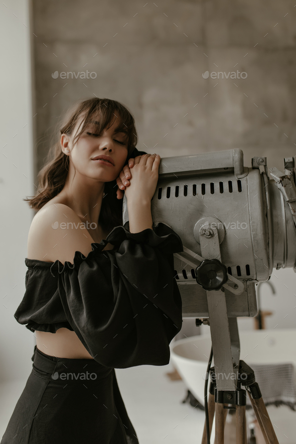 Calm brunette woman in cropped stylish blouse and black trendy skirt poses with closed eyes in apar
