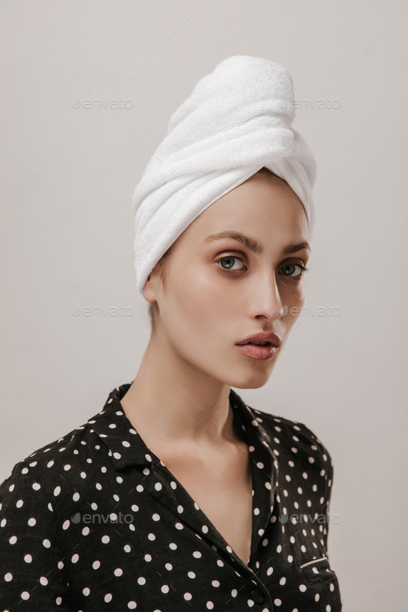 Engaging young girl in white towel on head and black polka dot pajama shirt, looking into camera se