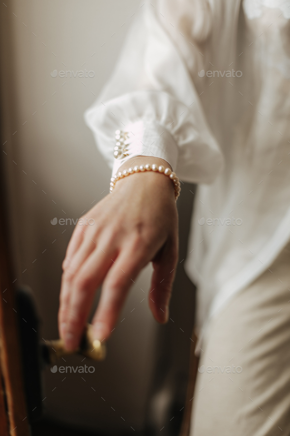 Photo of female hand with pearl bracelet inside. Girl in white modern blouse and beige trousers sho