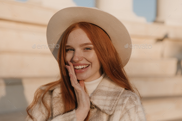 Fashion portrait of young lady smiling outdoors. Cute red-haired girl with nude makeup, plaid coat - Stock Photo - Images