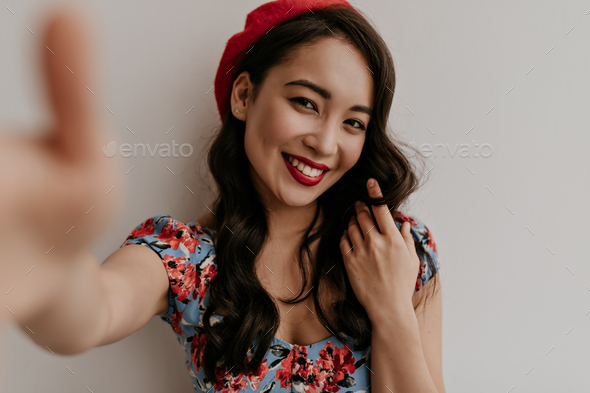 Tanned happy brunette woman in floral blouse and stylish bright beret takes selfie on isolated. Cha