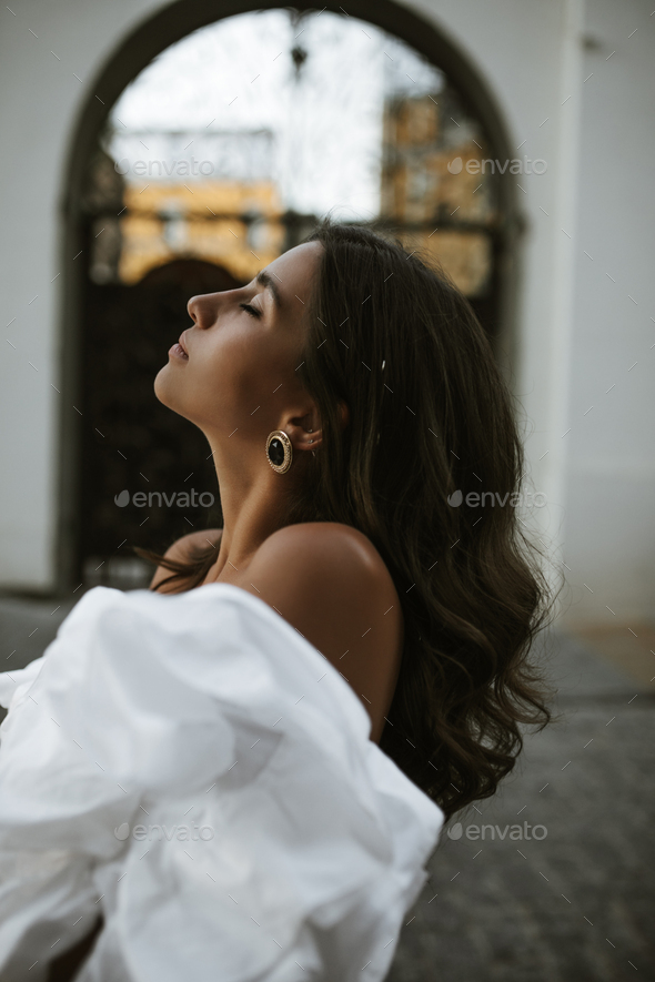 Profile portrait of elegant young brunette with long dark hair, closed eyes, tanned body in white o