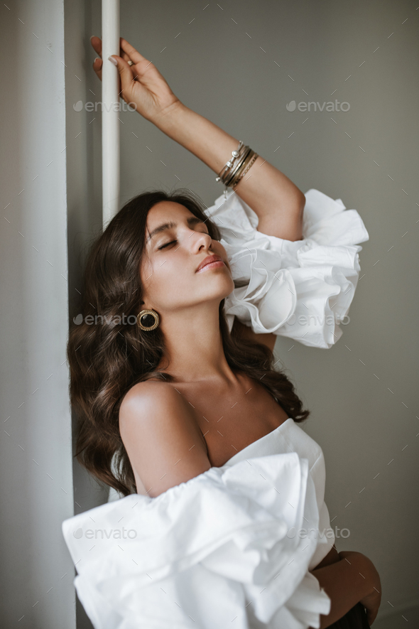 Beautiful young lady with curly brunette hair and stylish make-up, in white off-shoulder top, vinta