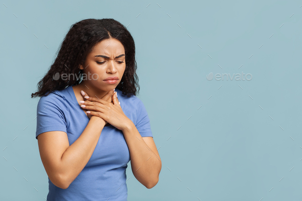 Upset african american woman suffering from acute pain in chest, feeling unwell over blue background