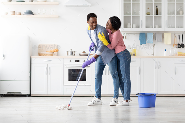 Positive black couple cleaning up together, vacuuming under carpet