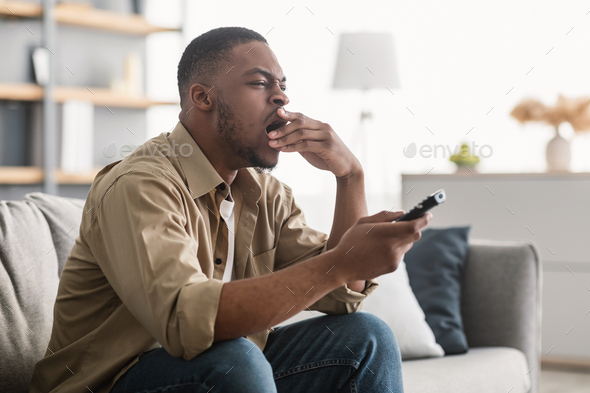 Bored Black Guy Yawning Watching TV Sitting On Couch Indoors