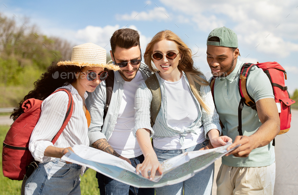 Local travel. Group of young people studying map on roadside, checking ...