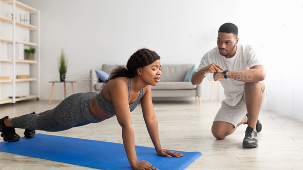 Young black lady having difficulty standing in plank for too long, her determined boyfriend noting