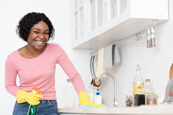 Positive black lady cleaning kitchen, erasing sink