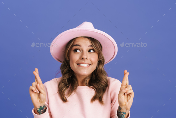 Happy charming girl in hat posing with fingers crossed for good luck