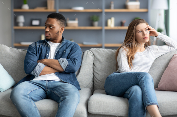 Relationship Crisis. Offended Interracial Couple Sitting On Couch After Quarrel