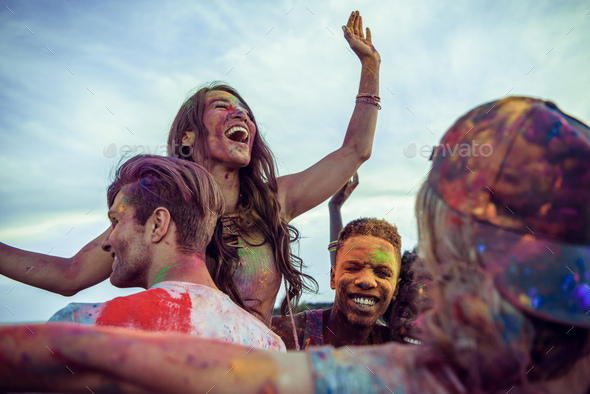 cheerful young multiethnic friends with colorful paint on clothes and bodies having fun together at