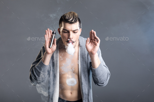 Young handsome man vaping and making smoke circles isolated on grey