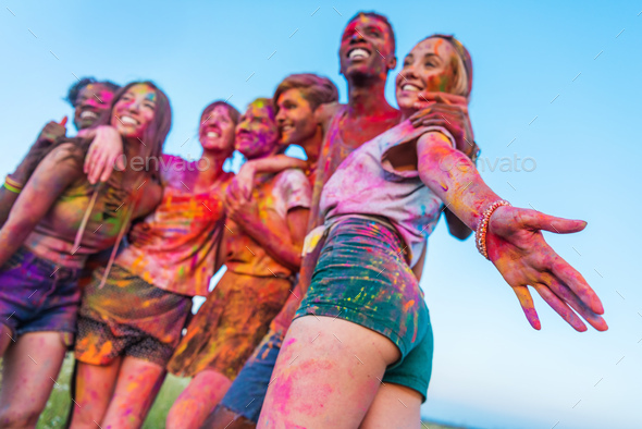 low angle view of happy young friends with colorful paint on clothes standing together at holi