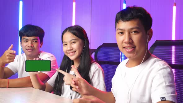 Team Of Asian Gamers Sitting On Chair And Pointing To Mock Up Green Screen Mobile Phone alt