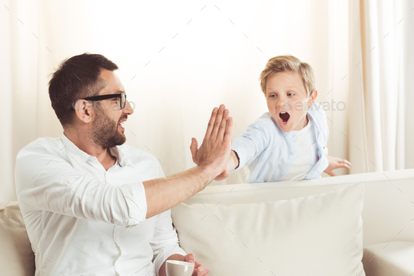 father drinking coffee and giving high five to his little son at home