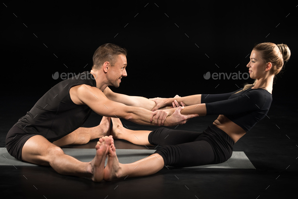 Couple performing acroyoga partner forward-fold exercise on yoga mat isolated on black