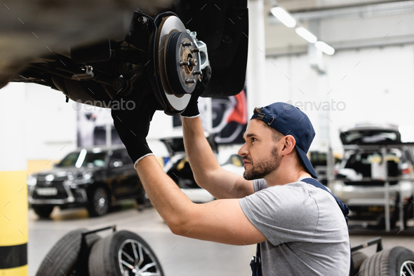 side view of mechanic in rubber gloves touching car brake and fixing ...