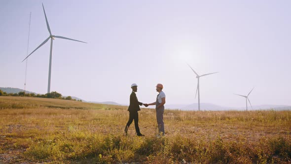 African Man in White Helmet and Black Suit Shaking Hands with Indian Engineer alt