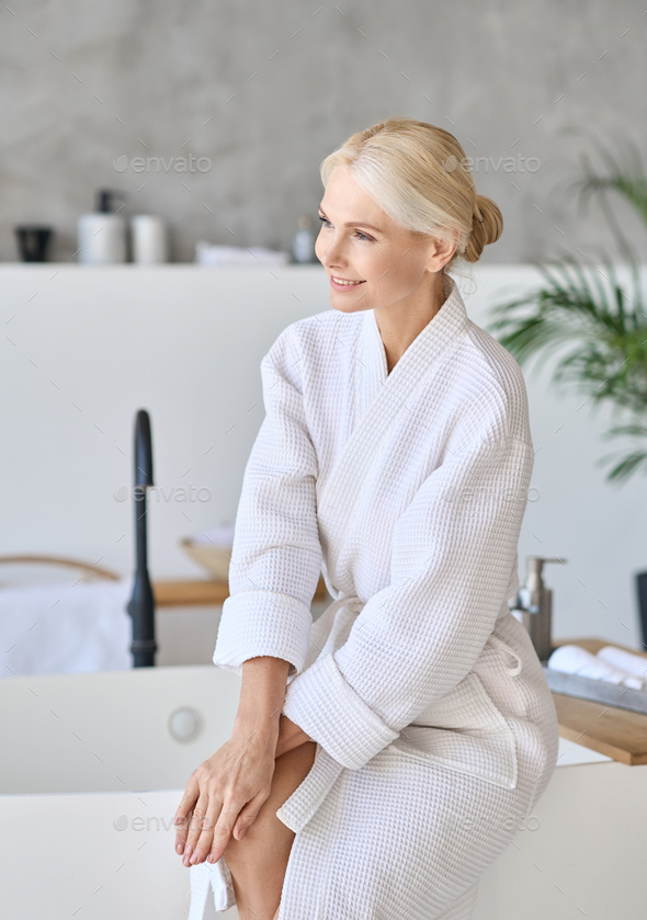 Portrait of smiling mid age woman sitting at spa center. Ads spa procedures.