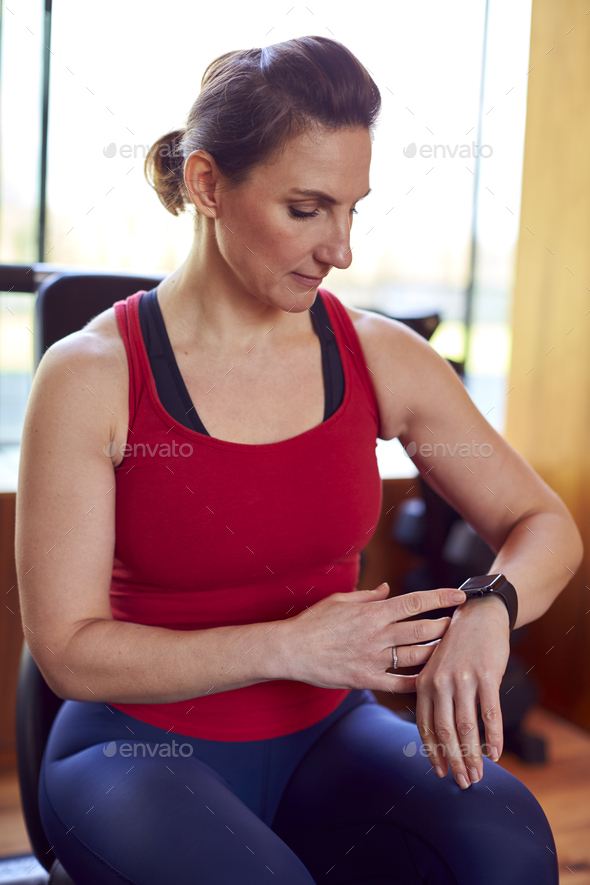 Mature Woman Exercising In Home Gym Checking Health App On Smart Watch  Stock Photo by monkeybusiness