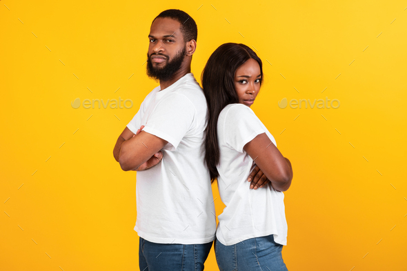 Afro couple standing back to back, yellow orange studio wall