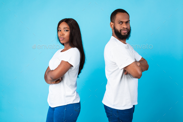 Afro couple standing back to back, blue studio background