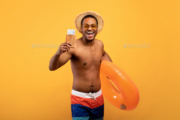Happy black guy holding inflatable ring, passport and tickets, going abroad to warm country