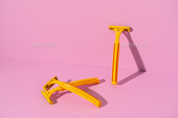 Yellow disposable razors on pink background, studio shot