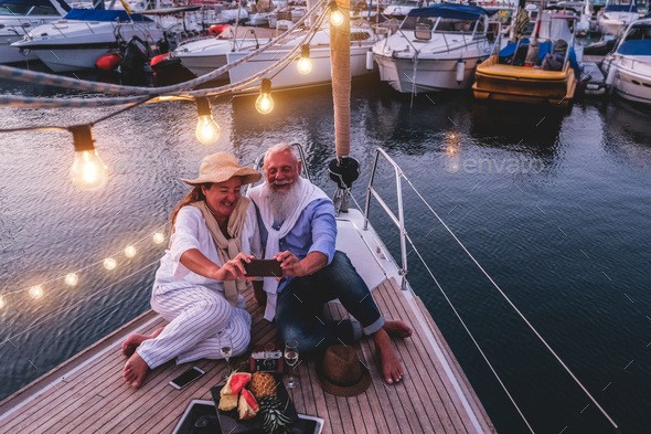 Happy senior couple taking selfie photo at night time on a sailboat, during anniversary vacation