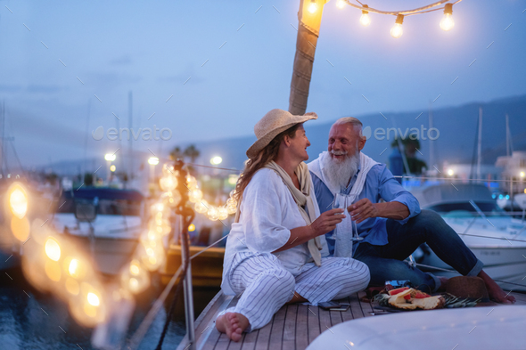 Senior couple cheering with champagne on a sailboat during wedding anniversary vacation - Stock Photo - Images