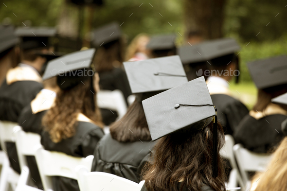 A group of students sit at a graduation ceremony, focus on mortarboard hat. - Stock Photo - Images