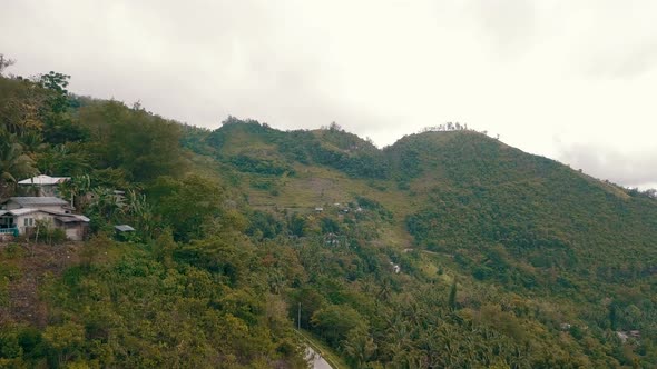 Aerial flying close to a mountainside with houses on it and covered by lush forest in central Cebu alt