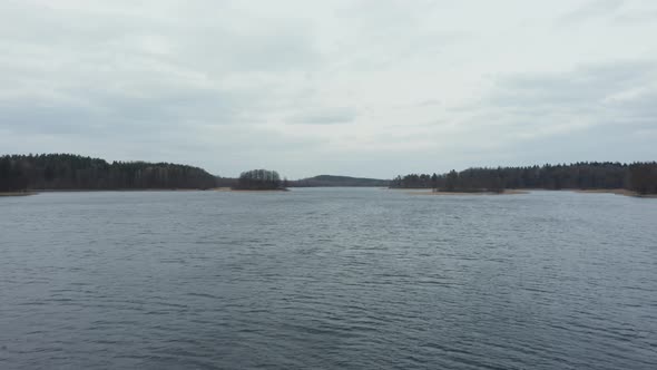 AERIAL: Rippling Water on the Surface of Lake with Forest in Background and Gloomy Sky in Horizon