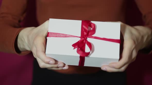 Beautiful Girl Holds Out a Gift in a White Box with a Red Ribbon