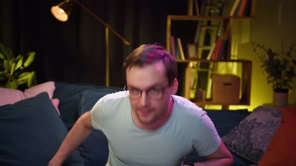 Young Man Sitting on Sofa and Playing Video Game on TV with Modern Console in Living Room alt