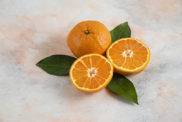 Whole and half cut clementine mandarins with leaves over colorful