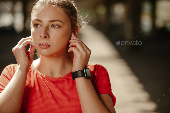 A blonde fitness girl with headphones in her ears, plays music on her phone and starts running.
