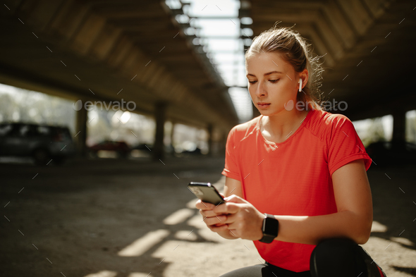 Fitness girl with headphones in ears, plays music on her phone and starts running around the city.