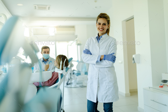 Dentist female with crossed arms wearing white coat posing and looking at camera. - Stock Photo - Images