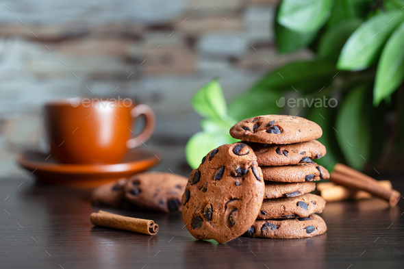 Oatmeal cookies with chocolate on the table against background of cup of coffee and green leaves - Stock Photo - Images