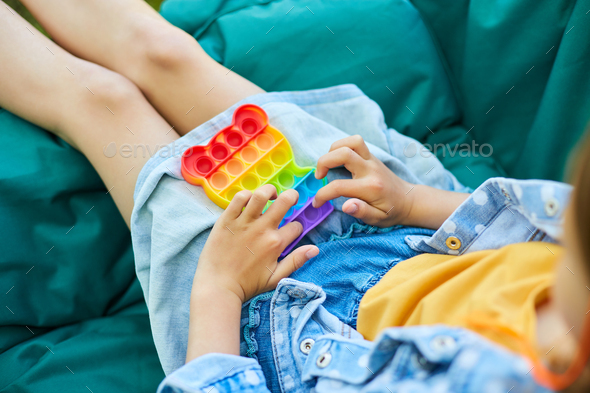 A little girl the on hanging chair outdoors play pop it, kid hands playing with colorful pop It - Stock Photo - Images