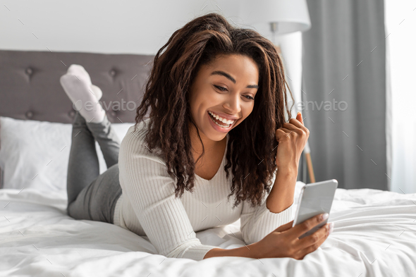 Excited black woman using phone shaking clenched fist