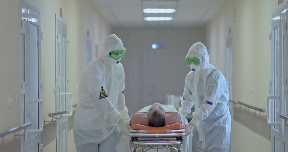 Doctors in Protective Suits Carry a Sick Patient on a Stretcher Along the Hospital Corridor alt