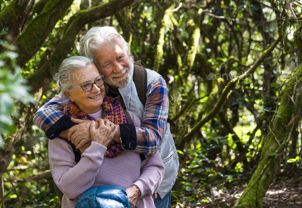 A senior couple tenderly embraced enjoying mountain hike in the woods among trunks and branches - Stock Photo - Images