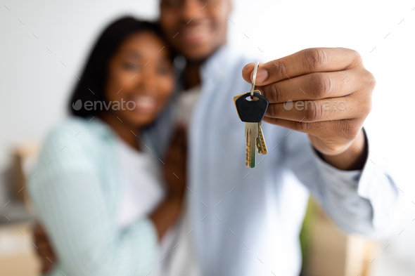 New home owners. Happy african american couple holding home keys,  celebrating buying new flat