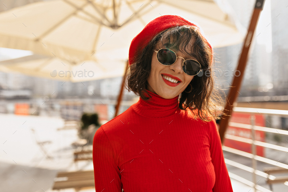 Outdoor portrait of attractive pretty girl with dark curly hair wearing  sunglasses and red beret Stock Photo by ansiia