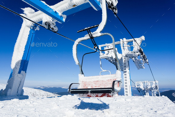 Empty ski lift covered with frost and snow with mountains at