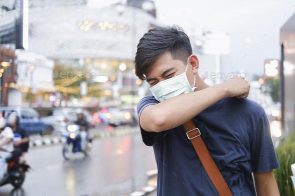 Close-up young man with protective face mask coughs in his elbow.