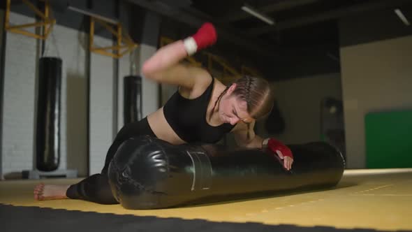 Kickboxing Aggressive Woman Fighter Trains His Punches Beats a Punching Bag While Lying on the Floor alt
